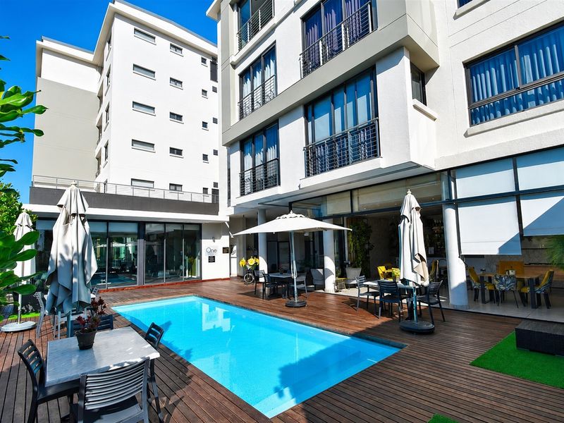Outdoor pool area featuring timber decking, modern apartment building facade, and large sliding glass doors leading to the interior living spaces.
