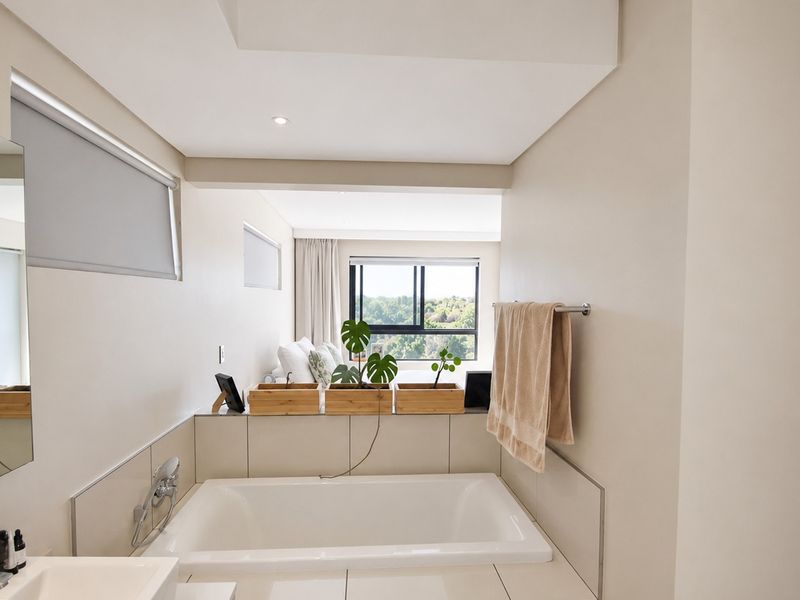 Modern bathroom featuring a built-in bathtub with tiled surround, towel rail, and a view through to the adjacent bedroom area.