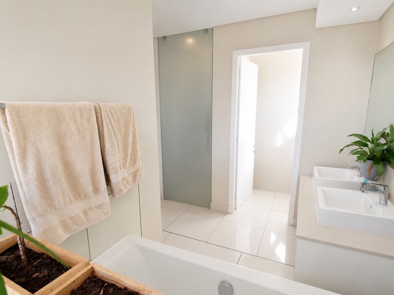 Modern bathroom featuring a double vanity with undermount sinks, tiled flooring, a built-in bathtub, and a frosted glass door leading to a separate area.