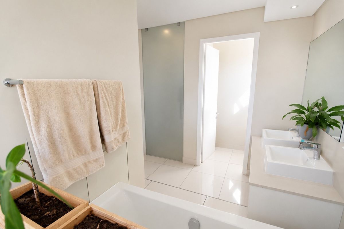 Modern bathroom featuring a double vanity with undermount sinks, tiled flooring, a built-in bathtub, and a frosted glass door leading to a separate area.