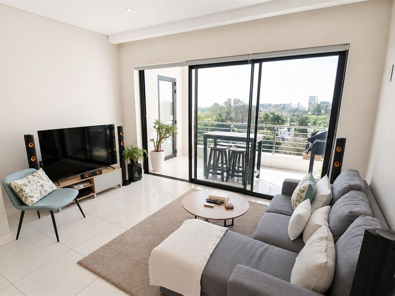 A bright and modern living room featuring large sliding glass doors that open onto a balcony, providing ample natural light and outdoor access.