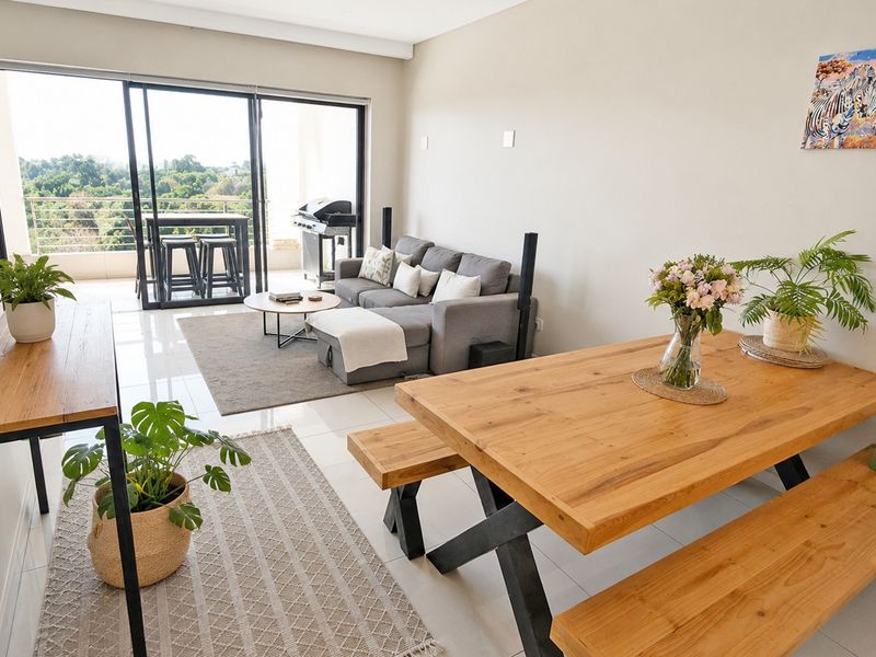 Bright open-plan living and dining area featuring large sliding glass doors that open onto a private balcony with scenic views.