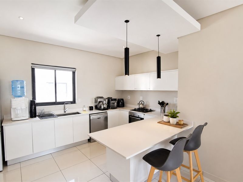 Modern kitchen featuring sleek white cabinetry, stone countertops, integrated appliances, a gas hob, and a functional breakfast bar with pendant lighting.