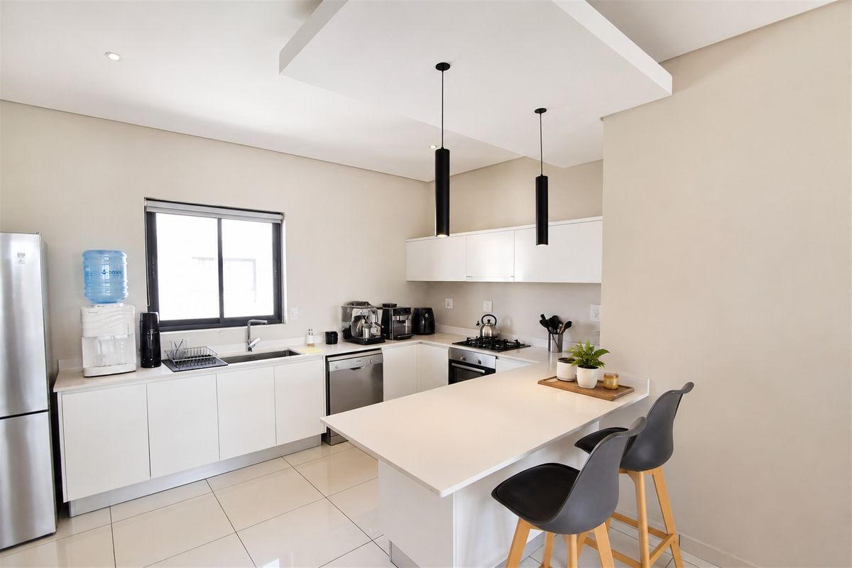 Modern kitchen featuring sleek white cabinetry, stone countertops, integrated appliances, a gas hob, and a functional breakfast bar with pendant lighting.