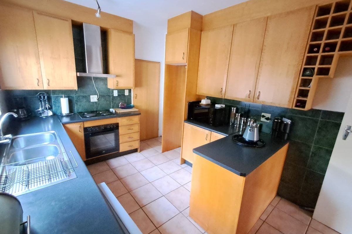 A functional kitchen featuring wooden cabinetry, dark laminate countertops, a built-in oven with extractor fan, and tiled flooring throughout.