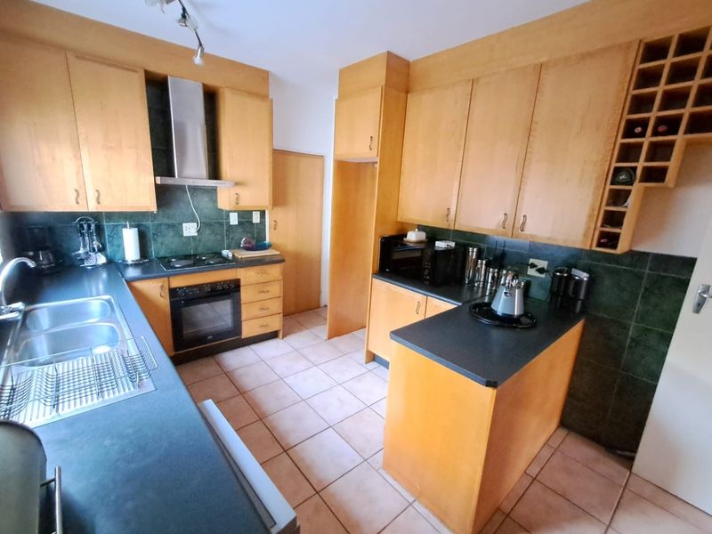 A functional kitchen featuring wooden cabinetry, dark laminate countertops, a built-in oven with extractor fan, and tiled flooring throughout.