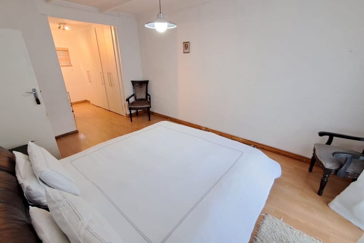 A bedroom featuring laminate flooring, built-in cupboards, and a pendant light fixture, with an adjoining walk-in closet area.