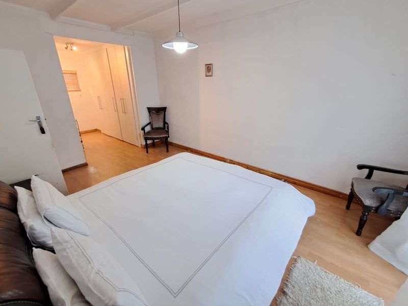A bedroom featuring laminate flooring, built-in cupboards, and a pendant light fixture, with an adjoining walk-in closet area.