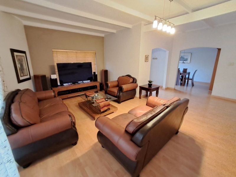 Spacious living room featuring exposed ceiling beams, laminate flooring, and an open-plan layout leading to the dining area.