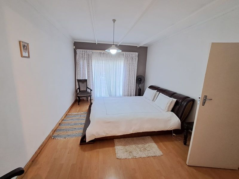 A spacious bedroom featuring laminate flooring, a central pendant light, and a sliding glass door providing access to the exterior.
