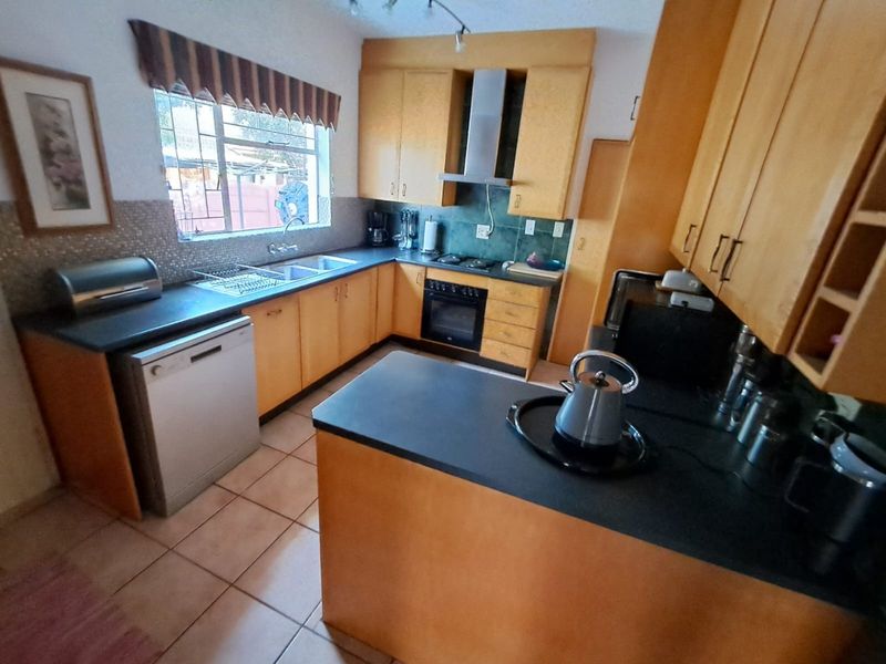 Functional kitchen featuring light wood cabinetry, dark countertops, built-in oven, extractor fan, and tiled flooring with a practical U-shaped layout.