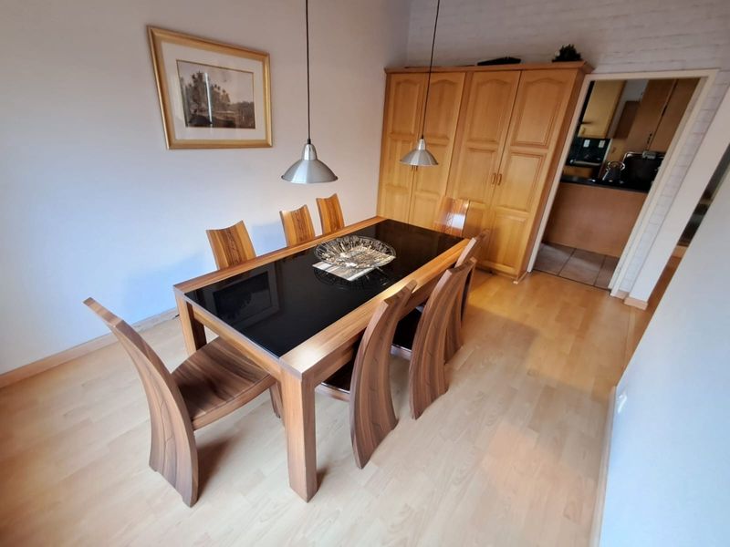 A dining room featuring light laminate flooring, built-in wooden cabinetry, and pendant lighting, with an adjacent view into the kitchen area.