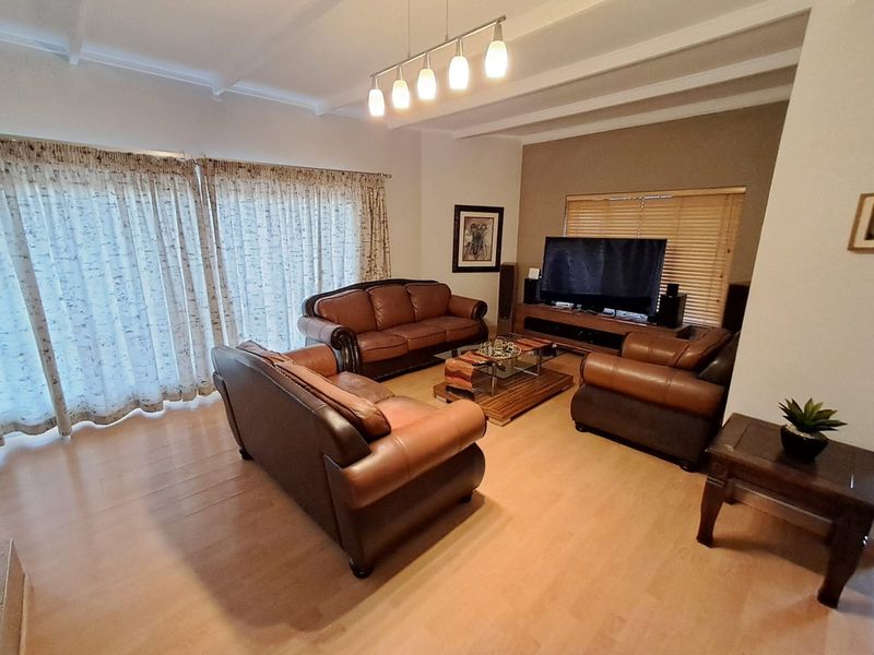 A spacious living room featuring laminate flooring, exposed beam ceilings, and large sliding glass doors that provide ample natural light.
