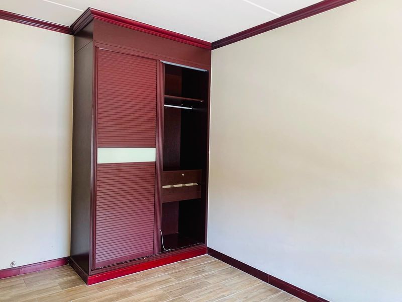 A bright, empty bedroom featuring tiled flooring, dark wood-toned built-in wardrobe, and matching crown molding and baseboards.