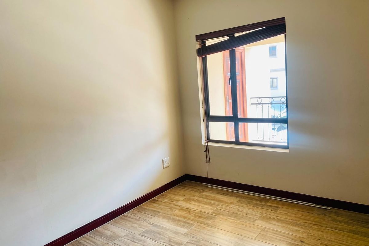 An empty bedroom featuring wood-look tiled flooring, dark timber skirting boards, and a window with an integrated blind.