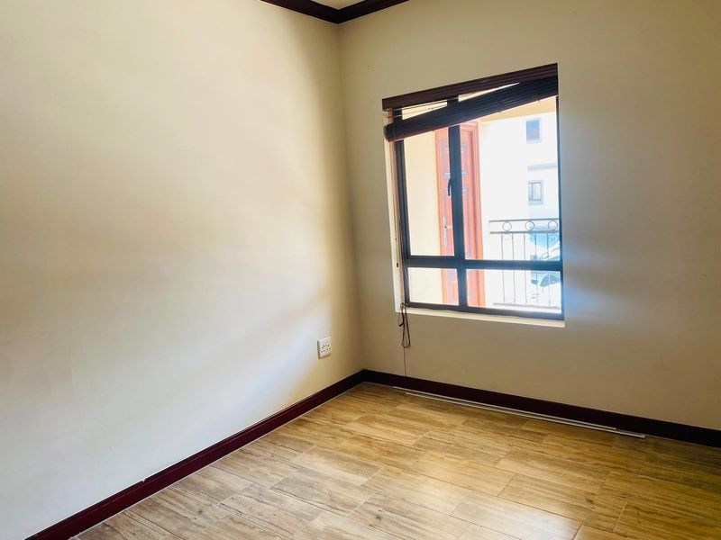 An empty bedroom featuring wood-look tiled flooring, dark timber skirting boards, and a window with an integrated blind.