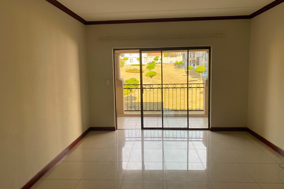 An empty, well-maintained living room featuring neutral tiled floors, crown molding, and a sliding glass door leading to a private balcony with garden views.