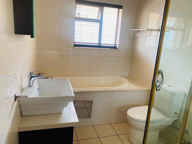 A functional bathroom featuring a built-in bathtub, separate shower enclosure, vanity basin, and toilet with neutral wall and floor tiling.