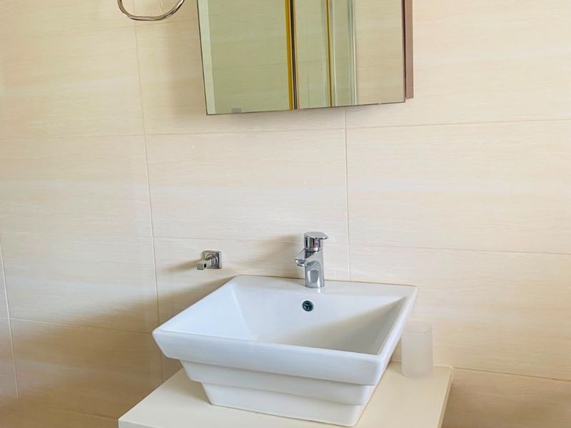 A clean and modern bathroom vanity featuring a white vessel sink, chrome faucet, and a mirrored medicine cabinet against neutral wall tiling.