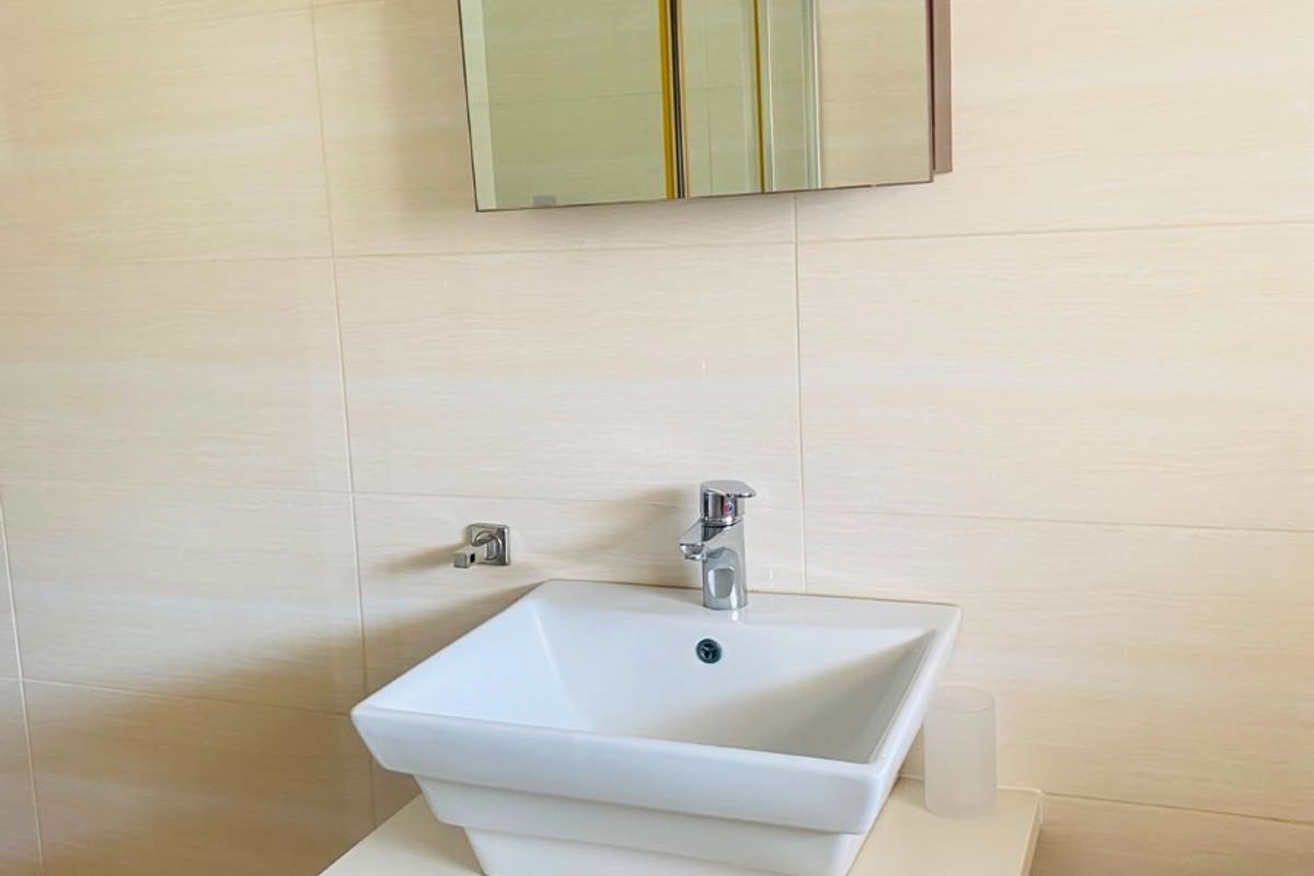 A clean and modern bathroom vanity featuring a white vessel sink, chrome faucet, and a mirrored medicine cabinet against neutral wall tiling.