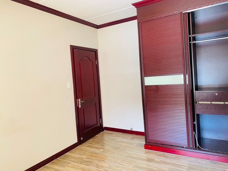 A clean, empty bedroom featuring tiled flooring, a dark wood built-in wardrobe, and matching timber door with decorative crown molding.
