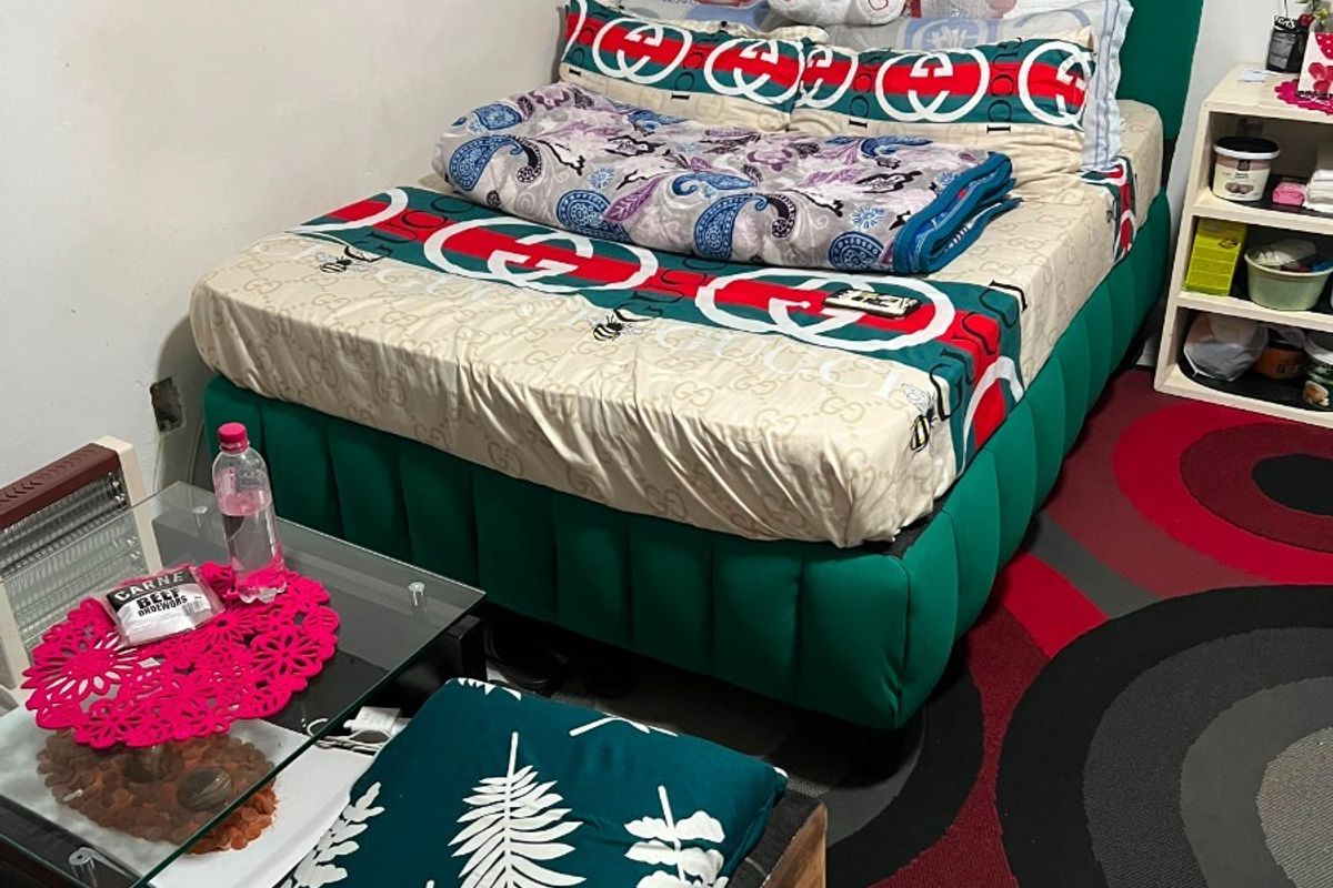 A compact bedroom featuring a green upholstered bed frame and built-in overhead shelving, finished with tiled flooring.