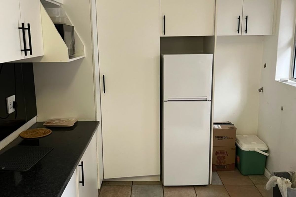 A functional kitchen featuring white cabinetry, black countertops, and tiled flooring, offering a practical layout with integrated storage solutions.