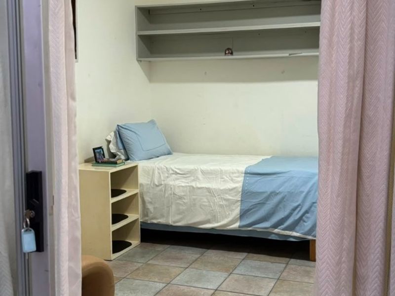 A functional bedroom featuring tiled flooring and built-in wall shelving, viewed through a doorway.