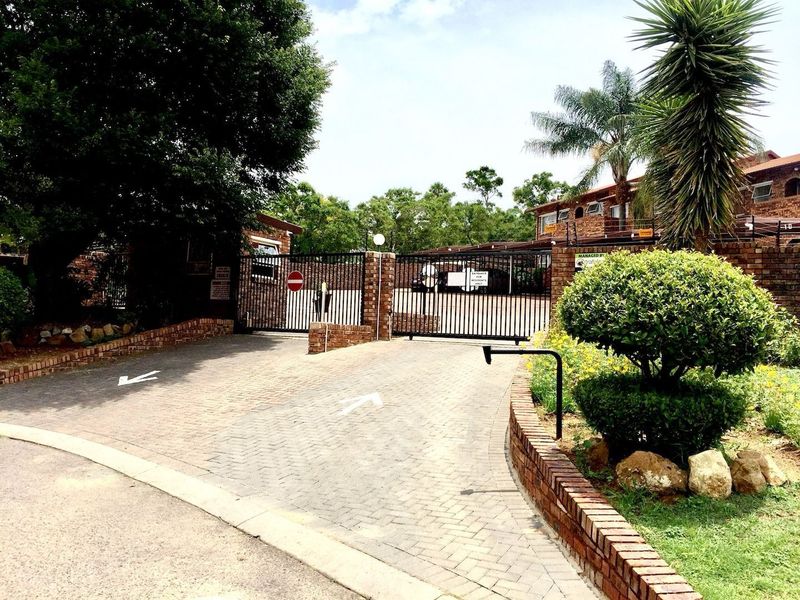 Front entrance view of the apartment complex featuring a secure gated access point with brick paving and perimeter security fencing.