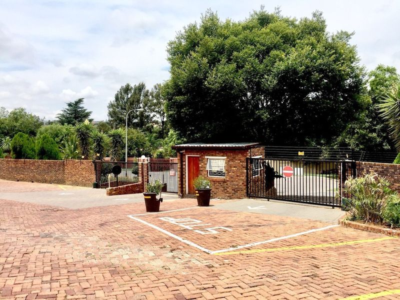 The entrance to the apartment complex features a brick guard house, secure metal gates, and a paved driveway area.