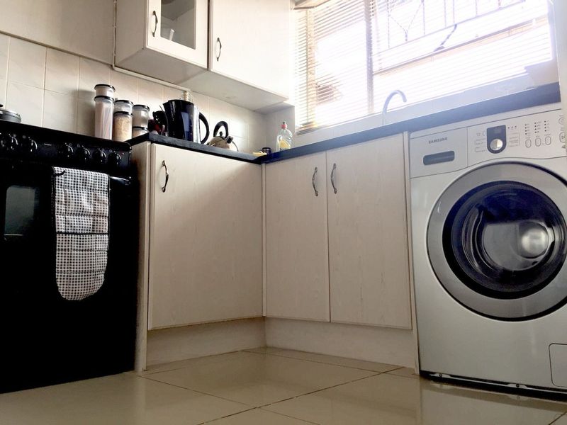 Compact kitchen featuring laminate cabinetry, tiled backsplash, dark countertops, and a dedicated space for a washing machine under the counter.
