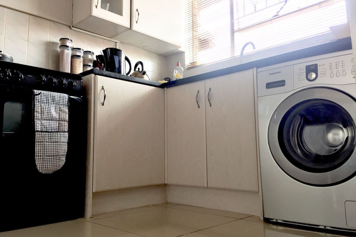 Compact kitchen featuring laminate cabinetry, tiled backsplash, dark countertops, and a dedicated space for a washing machine under the counter.