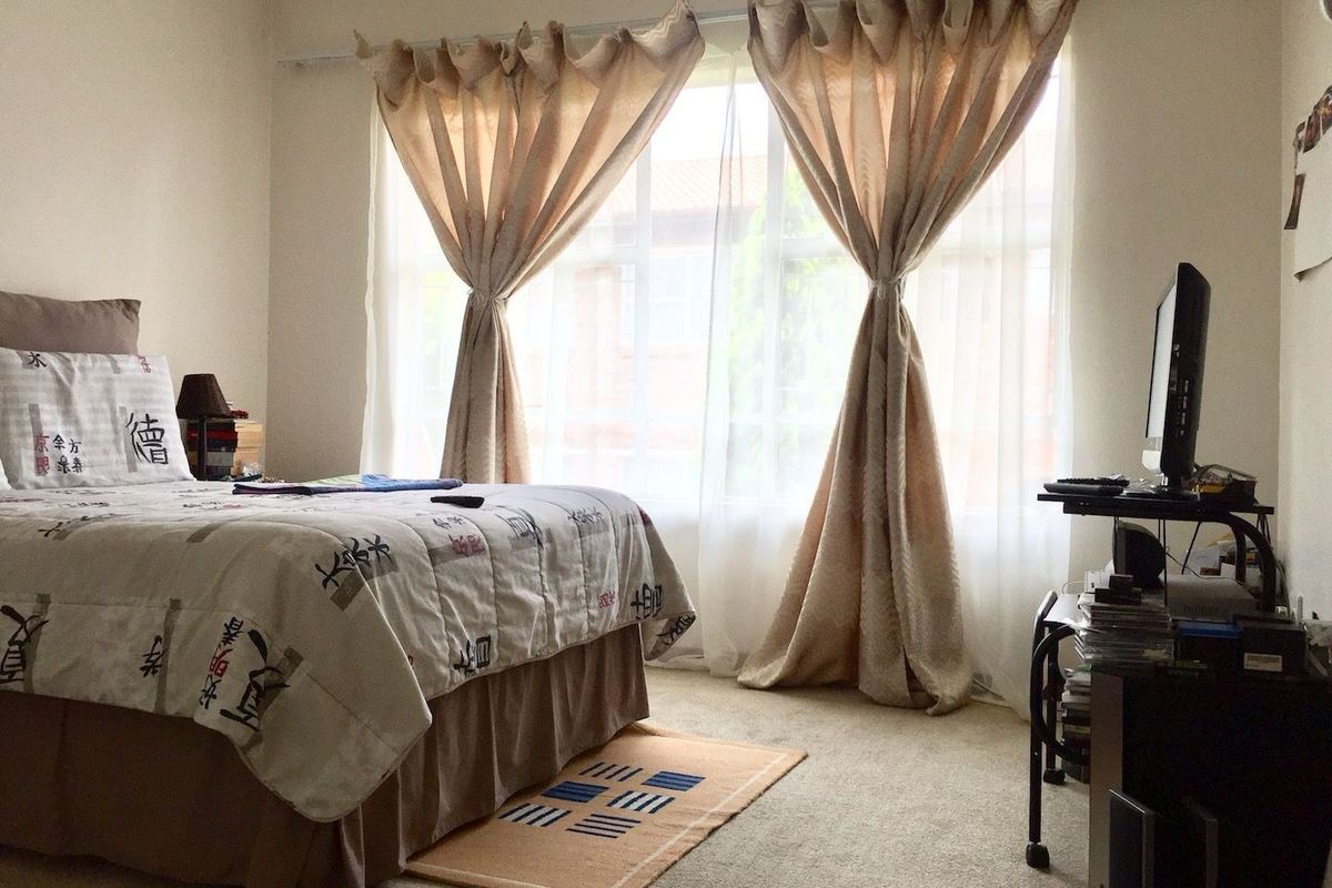 A standard bedroom featuring neutral wall tones, carpeted flooring, and a large window that provides natural light.