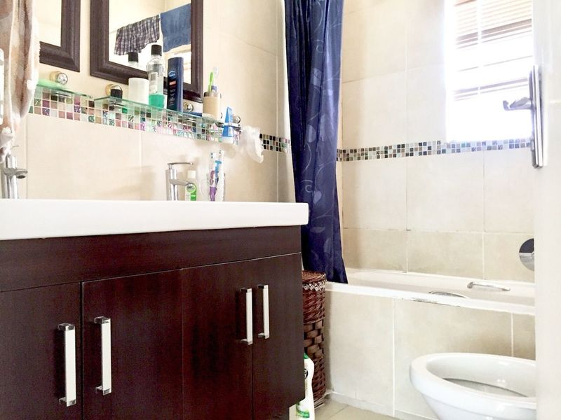 A functional bathroom featuring a dark wood vanity, bathtub with shower curtain, and neutral wall tiles with a decorative mosaic accent border.