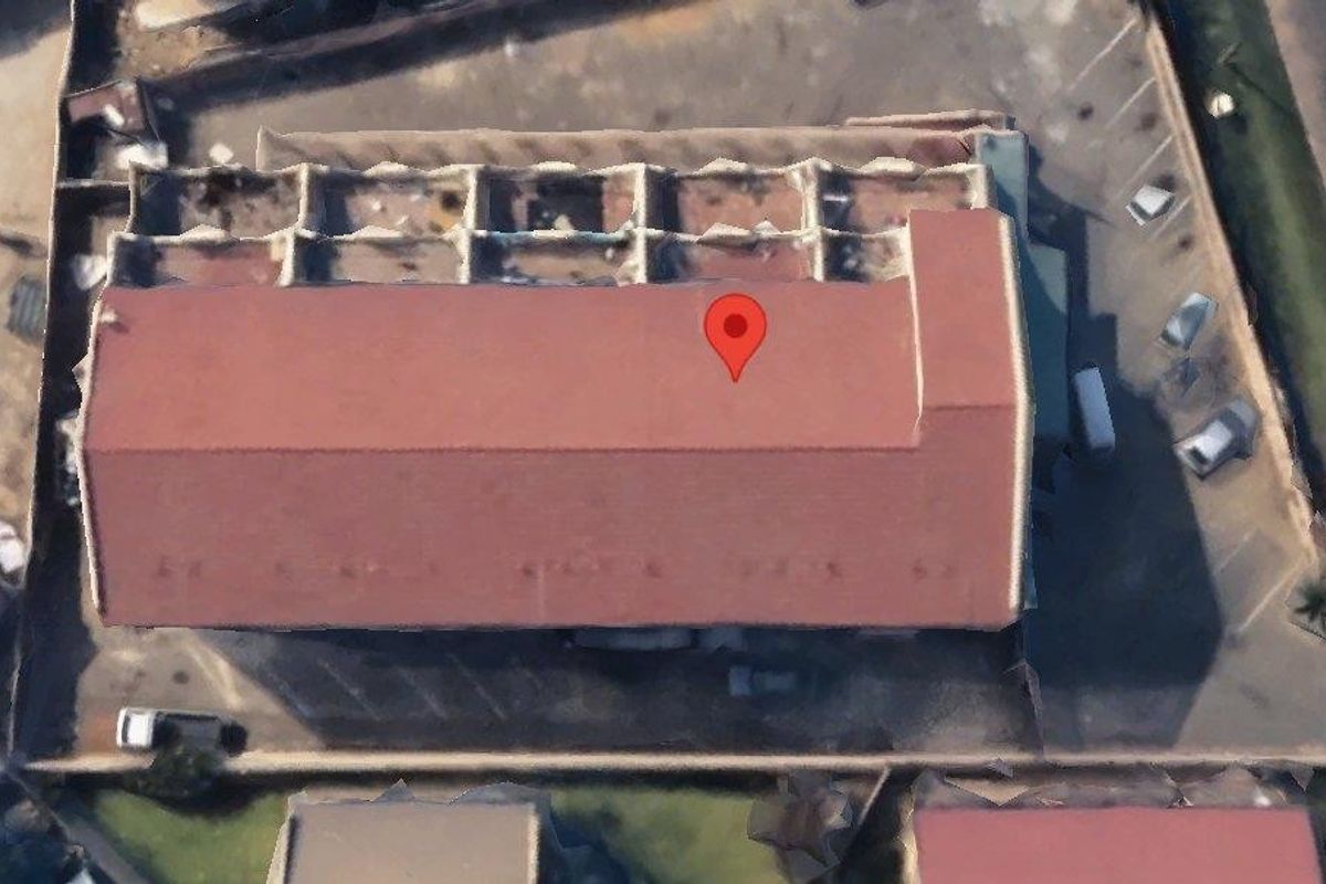 Aerial view of a commercial property featuring a pitched roof structure, perimeter boundary walls, and surrounding paved driveway area.
