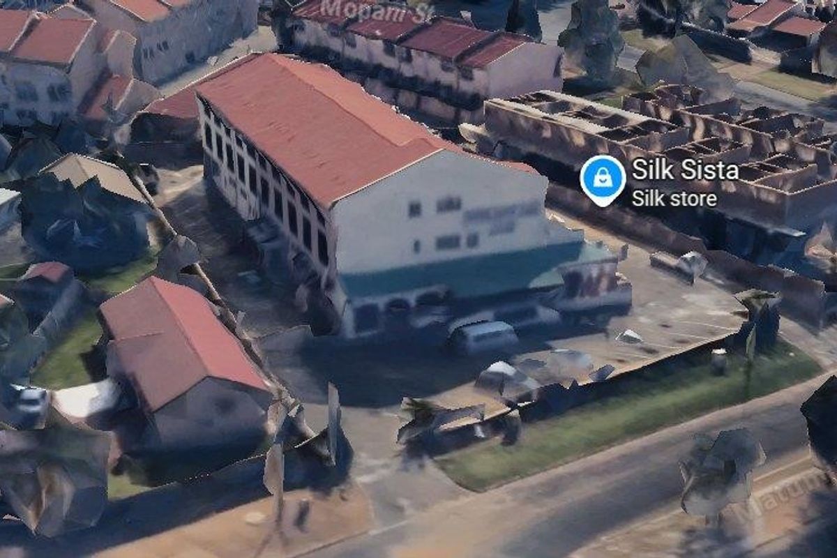 An aerial view of a commercial property featuring a multi-story building with a pitched roof and an adjacent paved parking area.