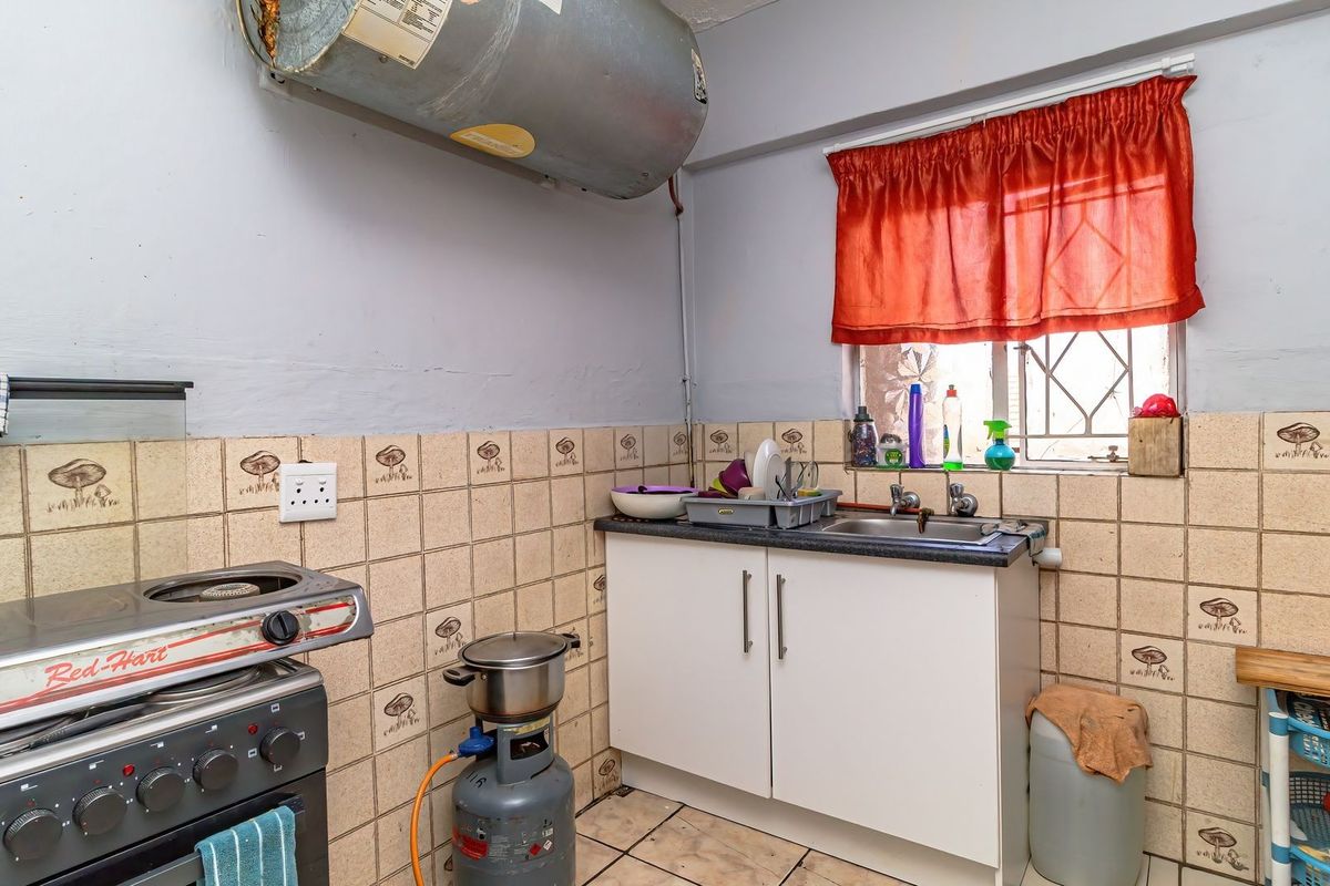 A compact kitchen area featuring tiled walls, base cabinetry, a stainless steel sink, and an exposed electric geyser unit.