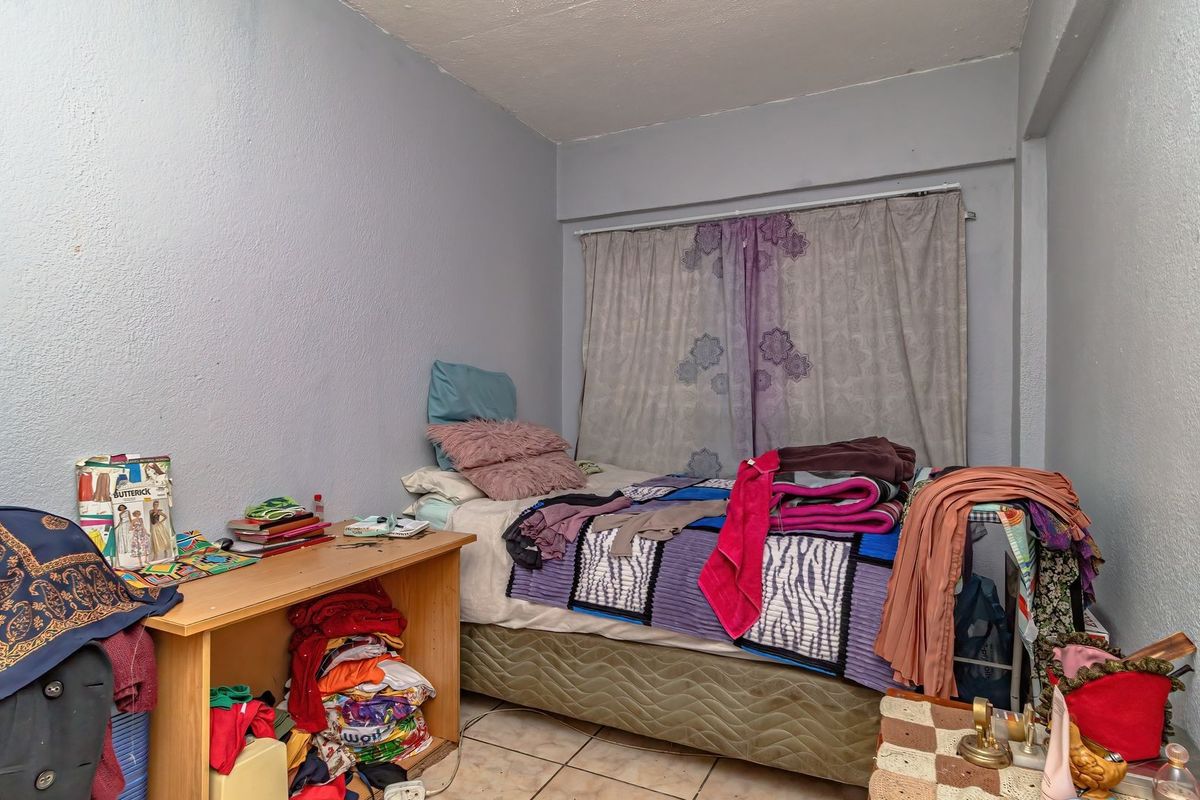 A compact bedroom featuring tiled flooring and neutral wall finishes, offering a functional space that could benefit from cosmetic updates and improved organization.