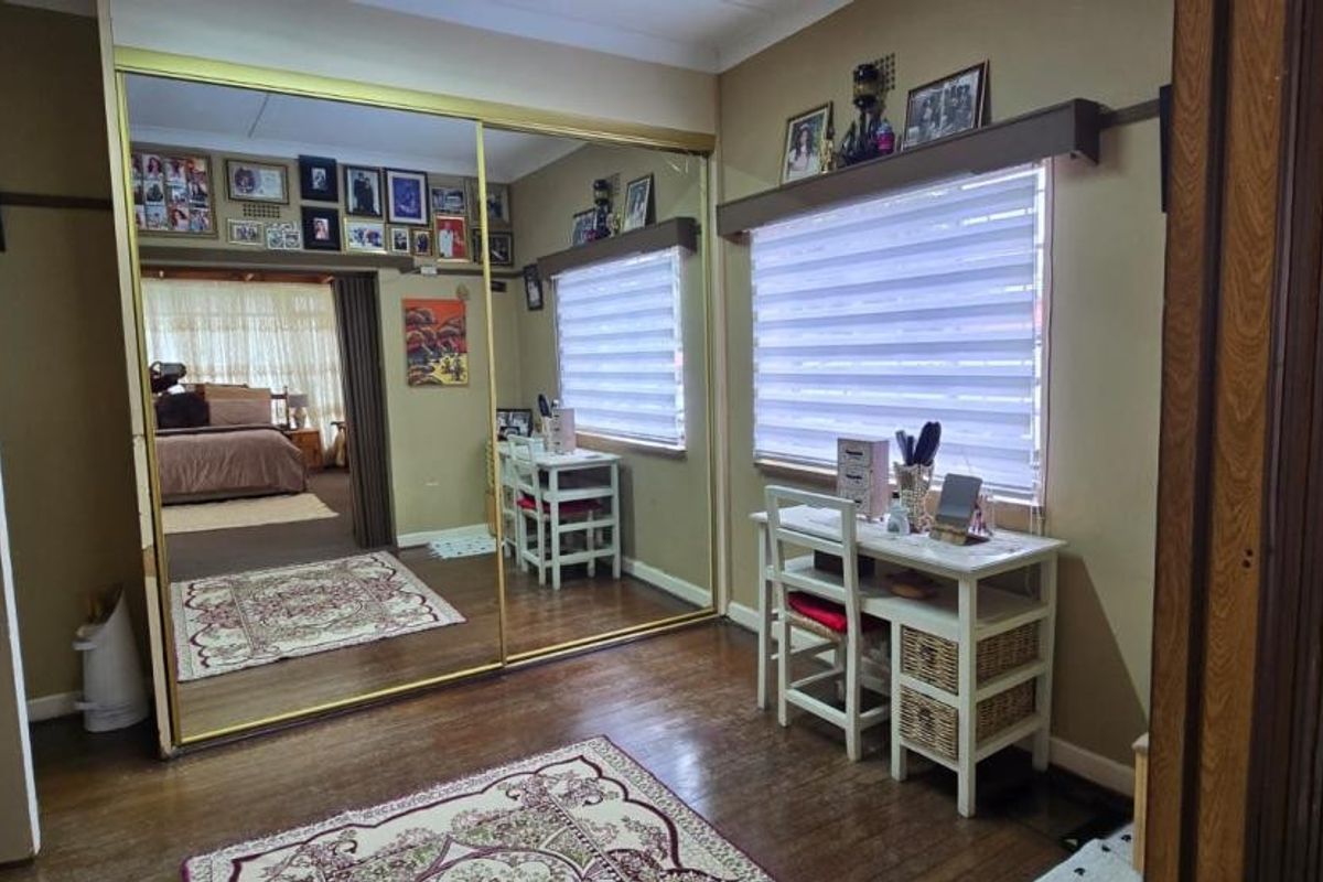Bedroom featuring timber flooring, large mirrored sliding wardrobe doors, and roller blinds, offering a functional space with classic finishes.