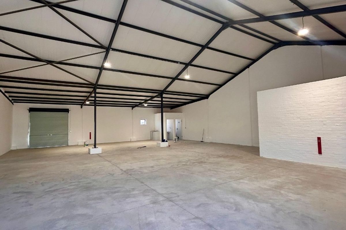 Spacious industrial utility space featuring high exposed steel truss ceilings, polished concrete flooring, and a large roller shutter door for easy access.