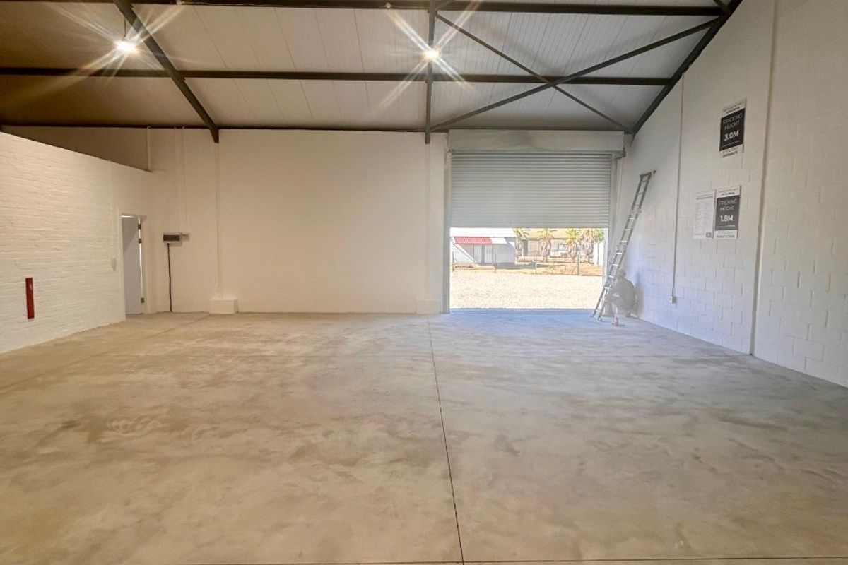 Spacious industrial utility space featuring high ceilings with exposed steel trusses, concrete flooring, and a large roller shutter door for easy access.
