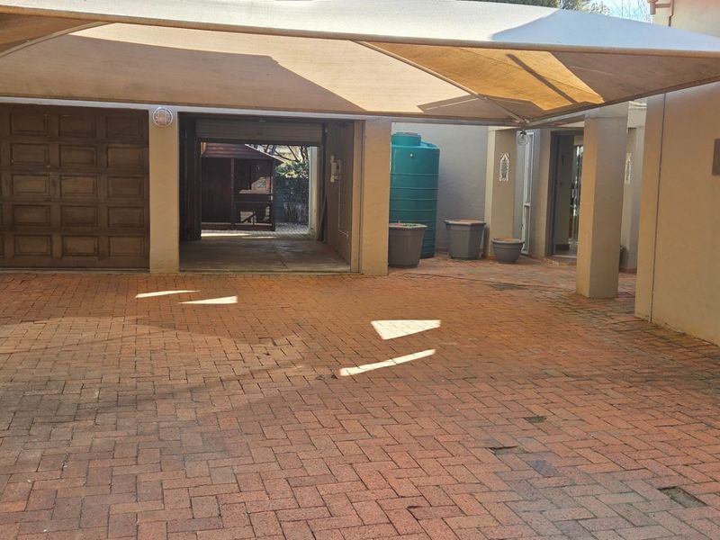 A paved driveway area featuring a large shade sail, integrated garage access, and a water storage tank.