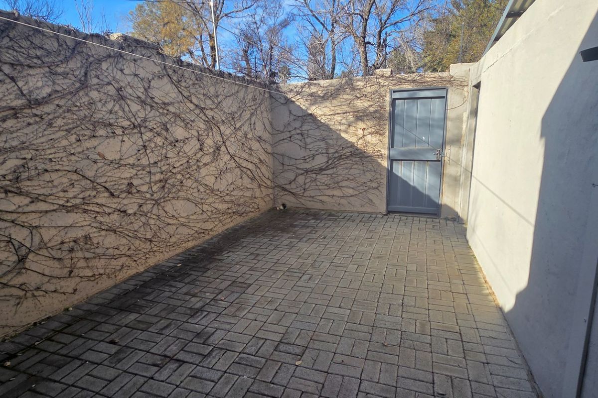 A private rear courtyard featuring paved flooring and high boundary walls with climbing vegetation, providing a secluded outdoor space.