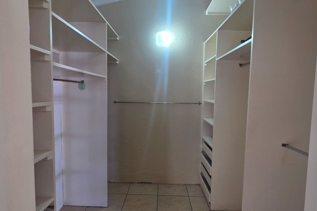 A walk-in closet or dressing area featuring built-in white cabinetry, shelving, hanging rails, and tiled flooring.