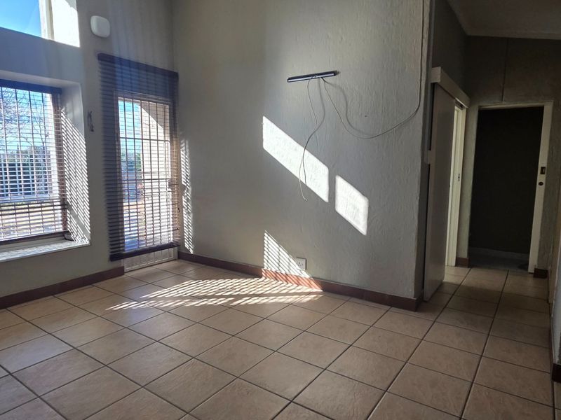 An empty living room featuring ceramic floor tiles, large windows with blinds, and a sliding door leading to the exterior.