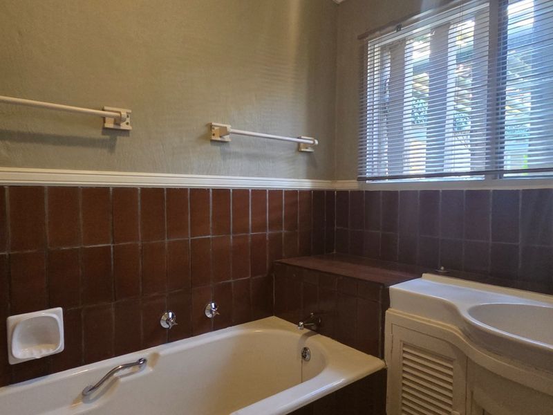 A dated bathroom featuring a built-in bathtub, vanity basin, and brown tiled splashback, offering potential for a modern renovation.