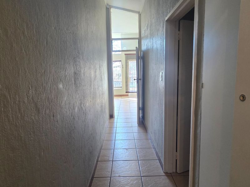 A narrow interior hallway featuring tiled flooring and access to adjacent rooms, leading towards a bright living area.