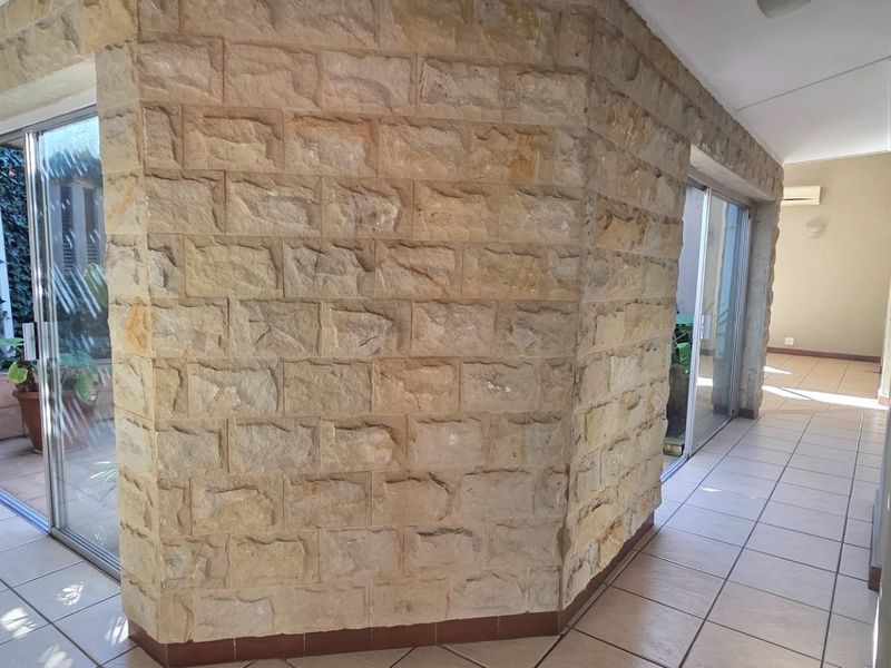 A spacious hallway featuring a prominent stone-clad feature wall, ceramic floor tiles, and large sliding glass doors providing access to outdoor areas.