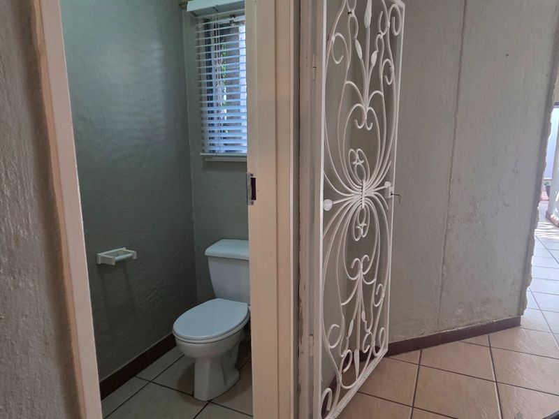 A compact guest bathroom featuring tiled flooring, a standard toilet, and a decorative security gate at the entrance.