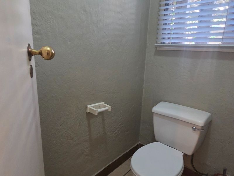 A compact bathroom featuring a standard toilet, tiled flooring, and window blinds.
